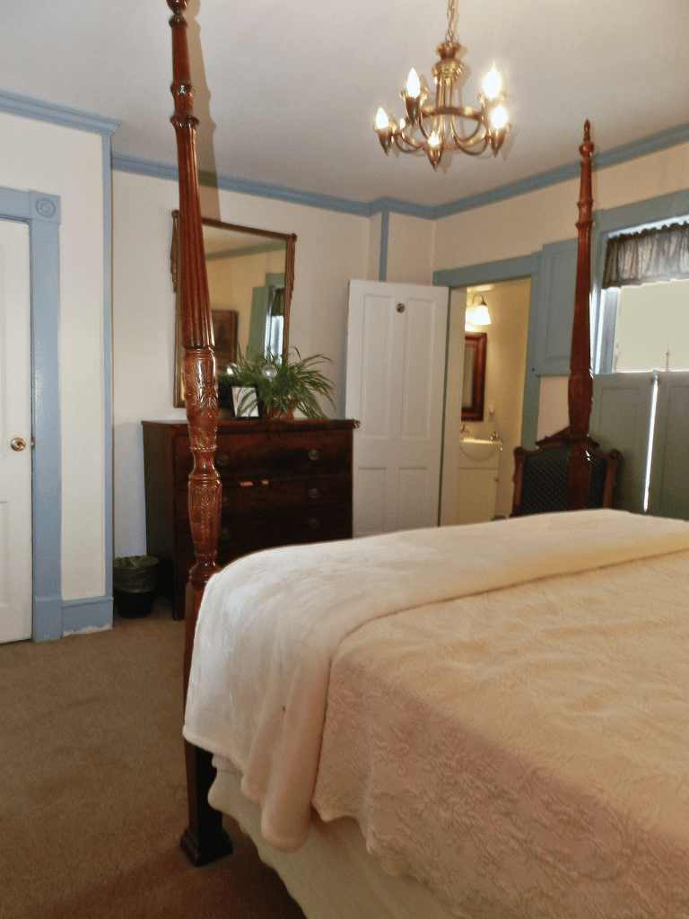 Queen bed with period-authentic wooden headboard in the Byrd Guest Room (Room 22) at The Historic Wayside Inn 1797, featuring historic decor and a private bathroom with shower in Middletown, VA.