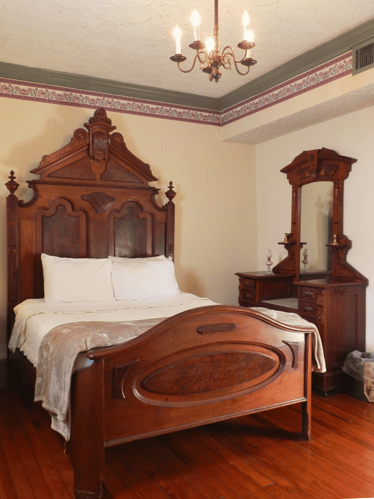 The Shenandoah Room (Room 18) featuring a queen bed with an ornate wooden headboard and a private bathroom with a shower at The Historic Wayside Inn 1797.