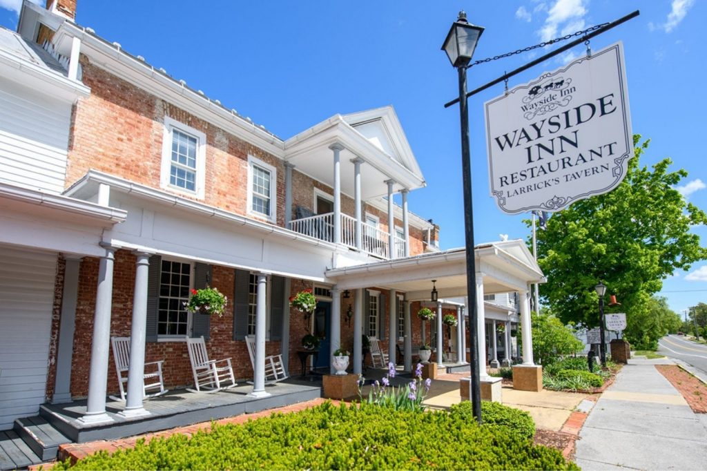 Alt Text Exterior view of The Historic Wayside Inn 1797 in Middletown, VA, showing the white pillared porch and historic architecture of America’s oldest continuously operating motor inn in the Shenandoah Valley.