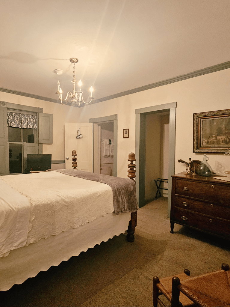 Queen-size bed with historic wood furnishings in the Wilson Room (Room 23) at The Historic Wayside Inn 1797, featuring a private full bathroom and authentic period decor in Middletown, VA.